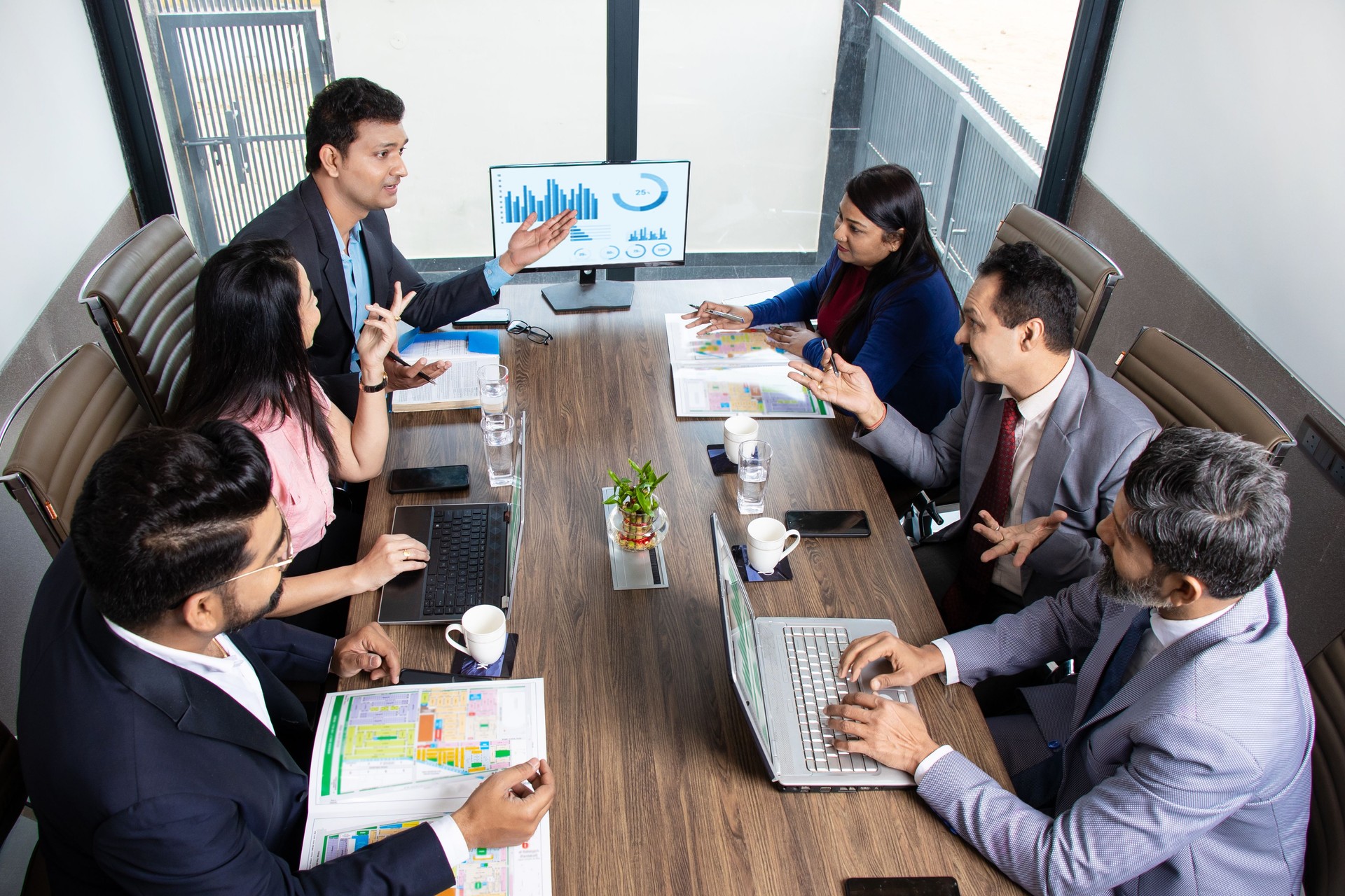 Indian business people meeting presentation in office conference room showing Charts Infographics on TV screen to show growth of company and big data analysis. E-Commerce e-Business. Top angle.